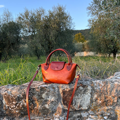 Floto Gattane Brown handbag on a stone wall with a natural landscape in the background